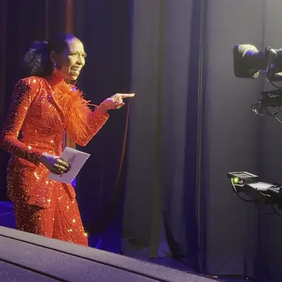 Looping clip: Chelsea in red sequins speaking on stage with cue cards as a broadcast camera rolls